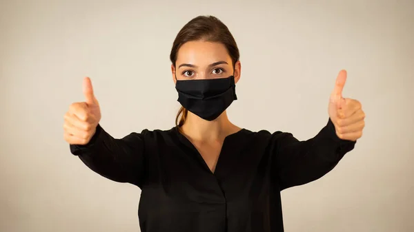 Positive woman wearing black face mask showing her thumbs up — Stock Photo, Image