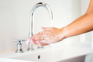 Kadın ellerini sabunla yıkıyor banyoda akan suyla.