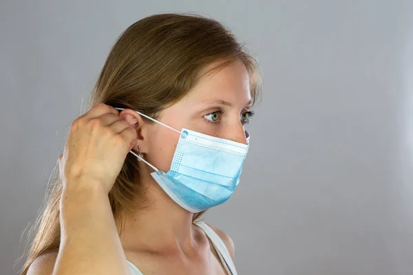 Young blond woman attaching surgical mask to her face — Stock Photo, Image