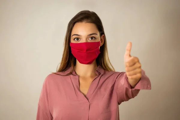 Positive young woman with red mask with thump up in studio — Stock Photo, Image