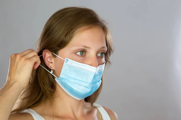 Female model in white shirt attaching surgical face mask on light background — Stock Photo, Image