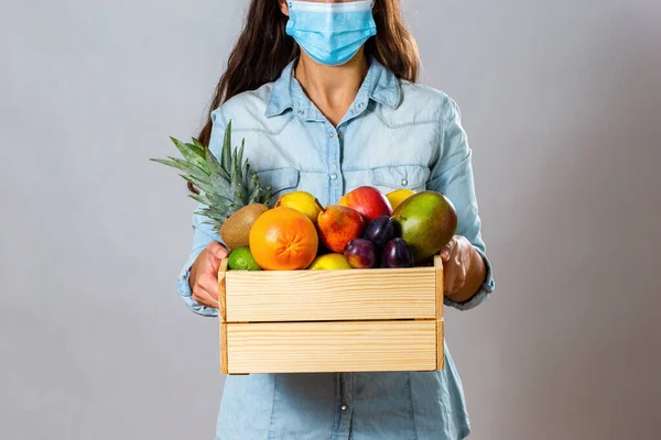 Brunette woman with surgical mask delivering box filled with fruit