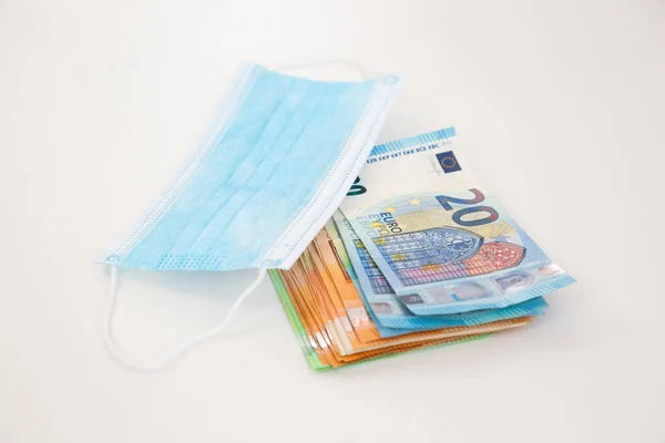 白いテーブルの上に青い外科マスクの下に横たわるユーロ銀行券のヒープ — ストック写真
