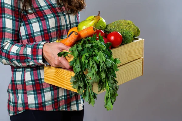 Person in flannel shirt holding box filled with fruit and vegetable