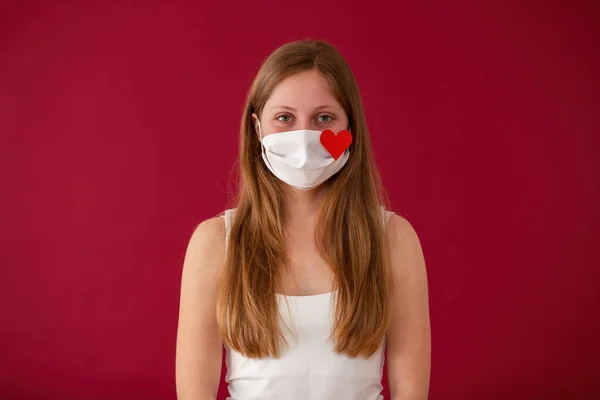 Woman wearing white cloth face mask and looking into camera from front view on red background. — Stock Photo, Image