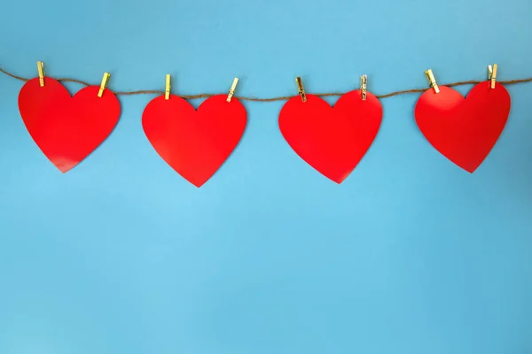 Čtyři červená srdce visí na šňůře na modrém pozadí s kopírovacím prostorem. — Stock fotografie