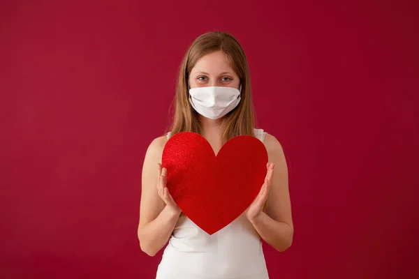 Smiling woman wearing face mask and holding red heart in hands. — Stock Photo, Image