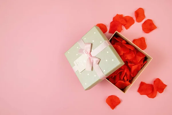 Open box filled with rose leaves on pink background — Stock fotografie