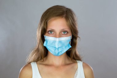 Cerrahi maskeli sarışın kadın stüdyoda kameraya bakıyor.