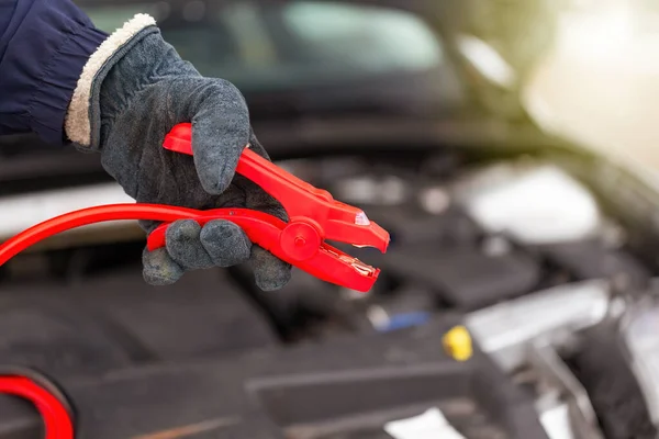 Людина тримає червоний джемпер кабель поруч з автомобілем крупним планом — стокове фото