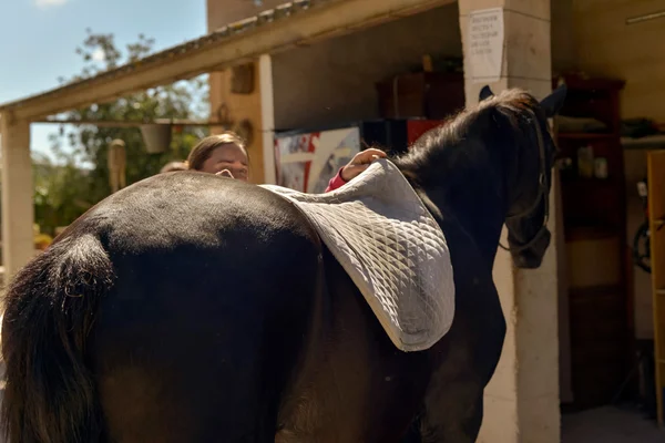 Jonge vrouw voorbereiding rug van paard — Stockfoto