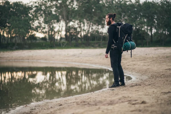 Skäggiga backpacker står vid sjön — Stockfoto