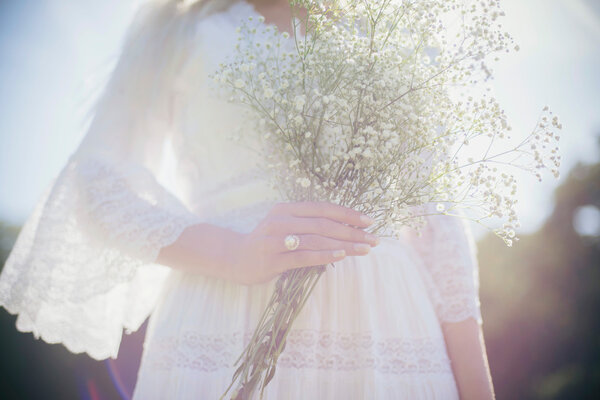 Close-up view of wedding ring on hand of bride holding white flowers outdoors