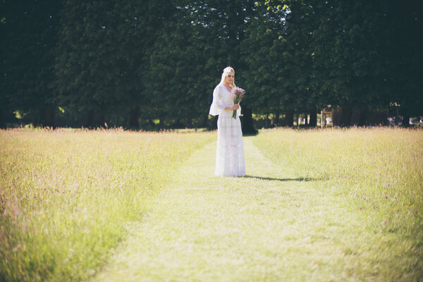Beautiful young blonde bride in white dress with bouquet standing on grass path
