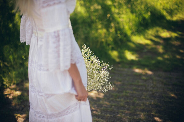 Rear view of blonde bride in white dress with flowers walking on path