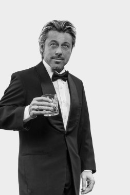 Smokinli ciddi bir adam beyaz arka planda bir bardak viski tutuyor. Siyah beyaz fotoğraf.