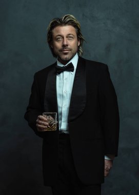 Smokinli sakallı, elinde viski bardağıyla mutlu sarışın adam..