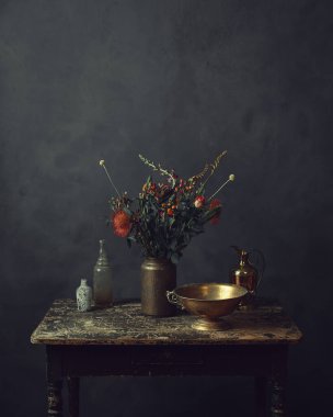 Üzerinde çiçekler, bronz bir kase, sürahi ve iki cam şişe olan eski ahşap bir masa..