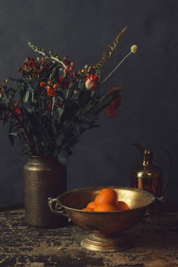 Üzerinde çiçekler olan eski ahşap bir masa, portakallı bronz bir kase ve bir sürahi..