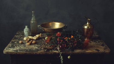 Bronz kaseli eski ahşap masa, zencefil ve ceviz, iki cam şişe, çiçekler ve bir sürahi..