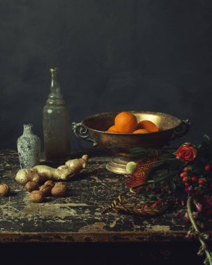 Portakallı, zencefilli ve cevizli bronz kaseli eski ahşap masa, iki cam şişe ve çiçek..