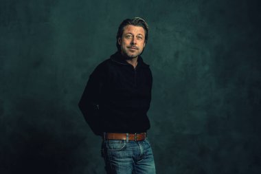 Gri duvara karşı siyah yün kazaklı sakallı bir adam..