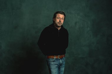 Gri duvara karşı siyah yün kazaklı sakallı bir adam..