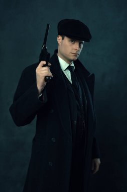 Siyah çizgili takım elbiseli, kepli, siyah duvarın önünde tabanca tutan tehditkar bir klasik adam.. 