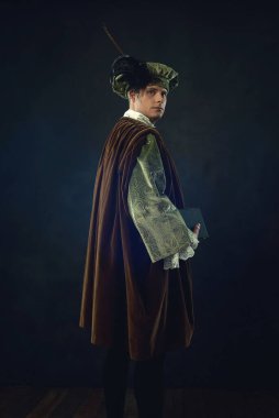 Elinde kitap tutan Rönesans adamı karanlık bir duvarın önünde duruyor..