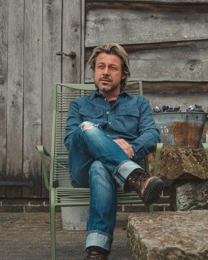 Blond man with beard sitting on terrace at farm in countryside.