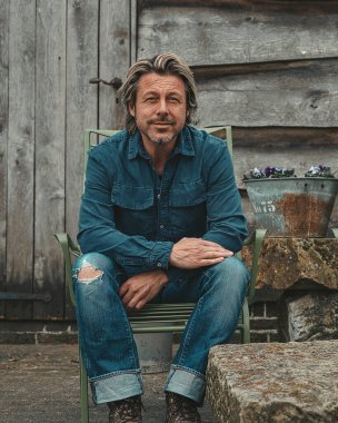 Blond man with beard sitting on terrace at farm in countryside.