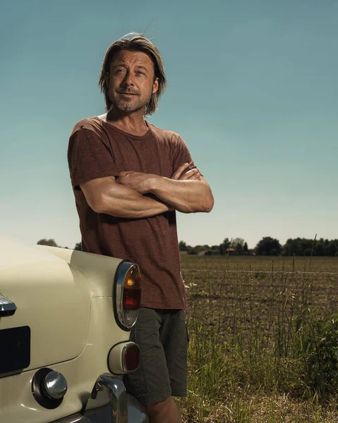Tシャツを着たブロンドの男と日当たりの良い田舎の古典的な車のトランクのそばに立つショートパンツ — ストック写真