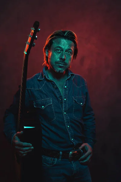 ジーンズのシャツにアコースティック西洋ギターを持つ男と赤と青の色の光でベルトを持つジーンズ — ストック写真