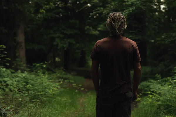穿着棕色T恤的金发男人走在森林小路上 后视镜 — 图库照片