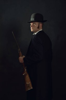 Koyu gri bir duvarın önünde elinde tüfekle Viktorya döneminden kalma bir adamın gölgeli portresi..