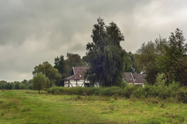 多云的天空下 长满了草原和树木的一片茂密的风景中 古老的半木质农舍 — 图库照片