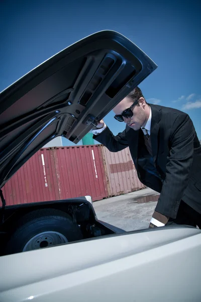 Retro fifties mafia fashion man looking in trunk of vintage car.