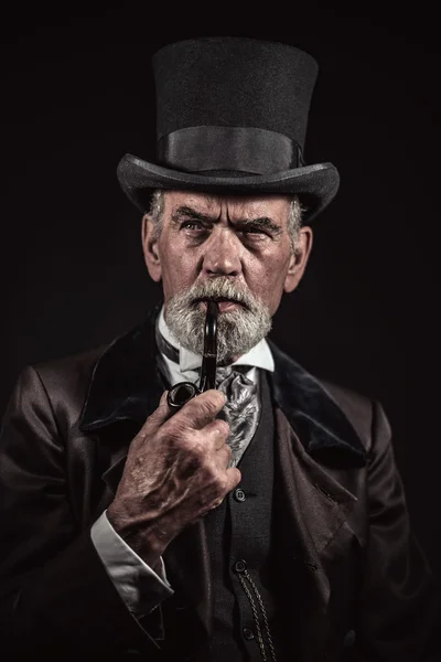 Pipe smoking vintage victorian man with black hat and gray hair — Stock Photo, Image