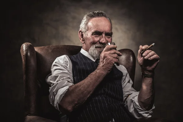 In chair sitting senior business man with cigar and whisky. Gray — Stock Photo, Image