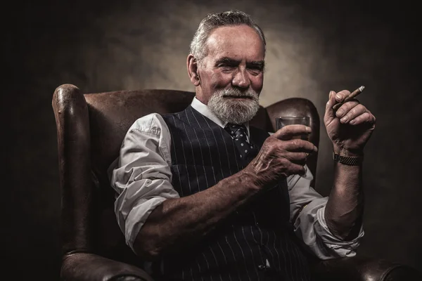 In chair sitting senior business man with cigar and whisky. Gray — Stock Photo, Image