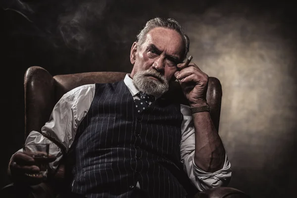 In chair sitting senior business man with cigar and whisky. Gray — Stock Photo, Image