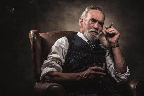 In chair sitting senior business man with cigar and whisky. Gray — Stock Photo, Image