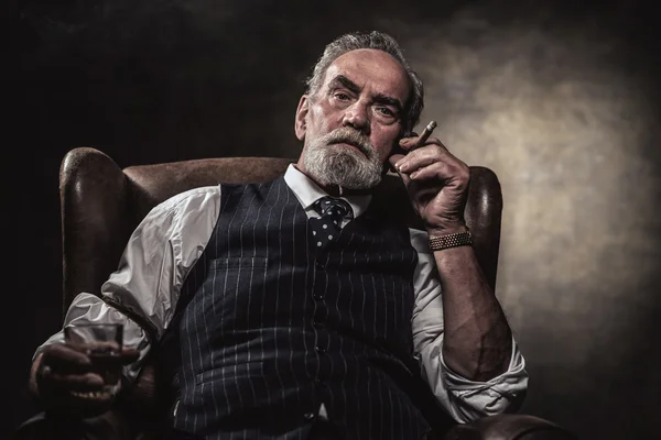 椅子に座って葉巻とウイスキーを持つシニア ビジネス男。グレー — ストック写真