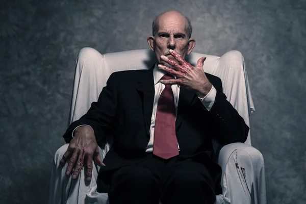 Malo hombre de negocios con manos ensangrentadas sentado en una silla blanca. Gris b — Foto de Stock