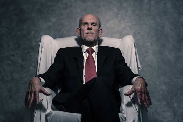 Bad businessman with bloody hands sitting in white chair. Gray b — Stock Photo, Image