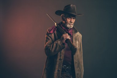 Old rough western cowboy with gray beard and brown hat holding r clipart