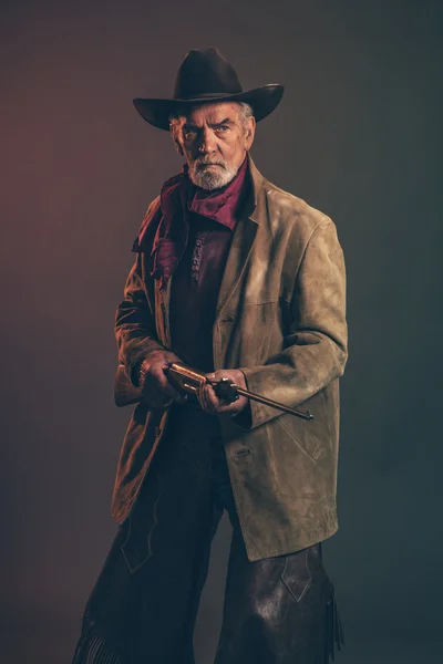 Starý hrubý západních kovboj s šedou bradkou a hnědý klobouk drží r — Stock fotografie