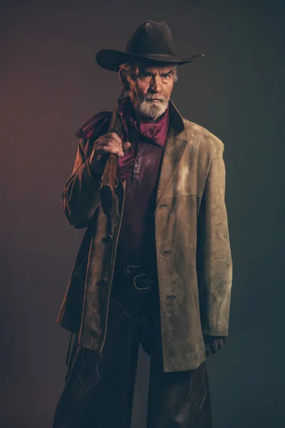 Old rough western cowboy with gray beard and brown hat holding r — Stock Photo, Image