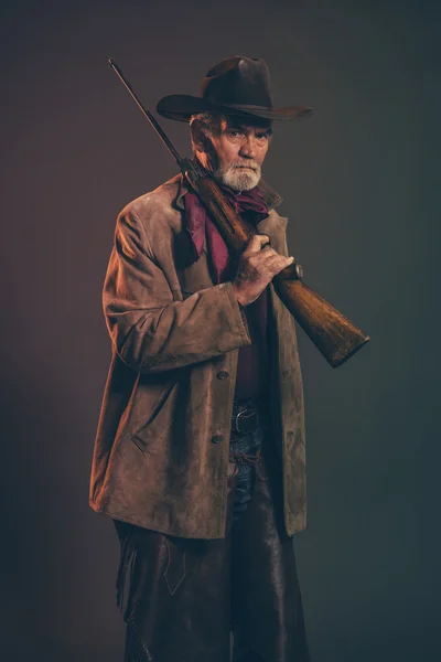 Velho cowboy ocidental áspero com barba cinza e chapéu marrom segurando r — Fotografia de Stock