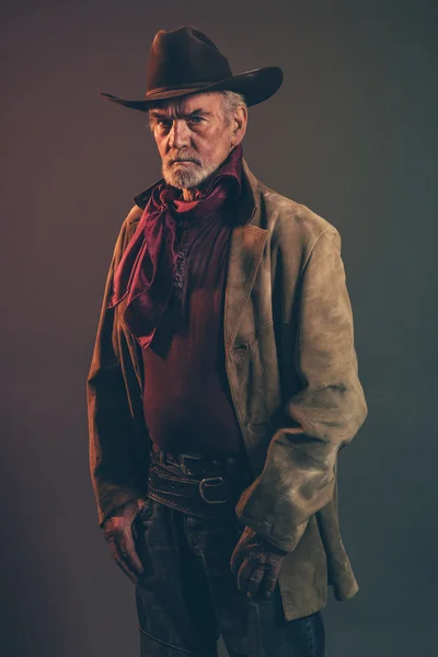 Old rough western cowboy with gray beard and brown hat. Low key — Stock Photo, Image